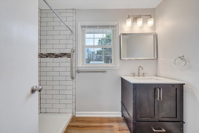 bathroom with tiled shower, vanity, baseboards, and wood finished floors