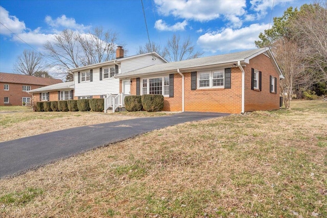 split level home featuring brick siding, driveway, a chimney, and a front lawn