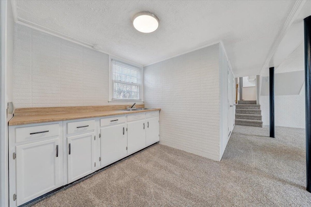 kitchen featuring a textured ceiling, light colored carpet, brick wall, a sink, and white cabinets