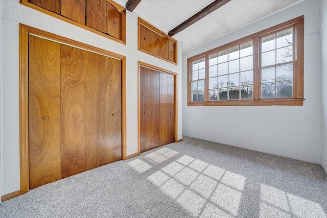 unfurnished bedroom with carpet floors, beam ceiling, and multiple closets