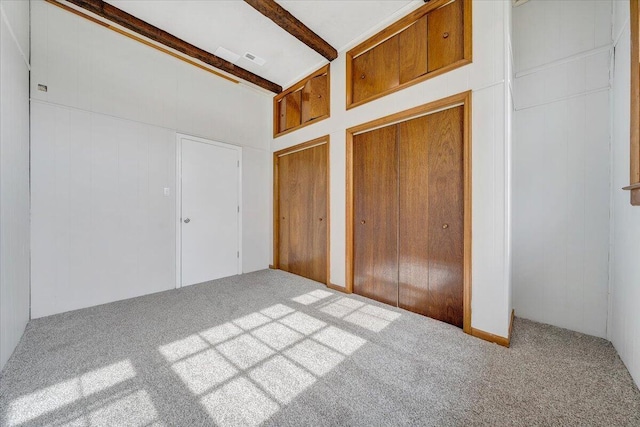 unfurnished bedroom with multiple closets, carpet flooring, and beamed ceiling