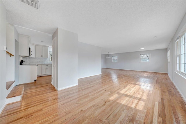 unfurnished living room featuring visible vents, baseboards, stairs, a textured ceiling, and light wood-type flooring