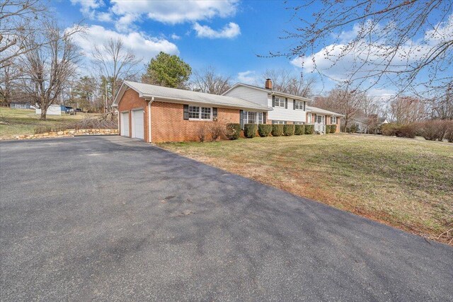 view of front of house with aphalt driveway, a garage, brick siding, a chimney, and a front yard