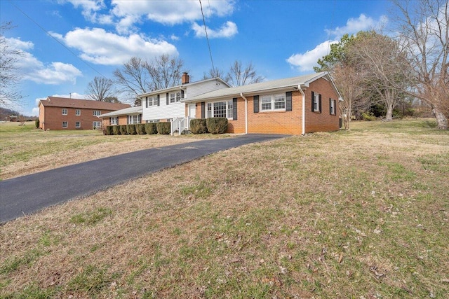 split level home with driveway, a chimney, a front lawn, and brick siding