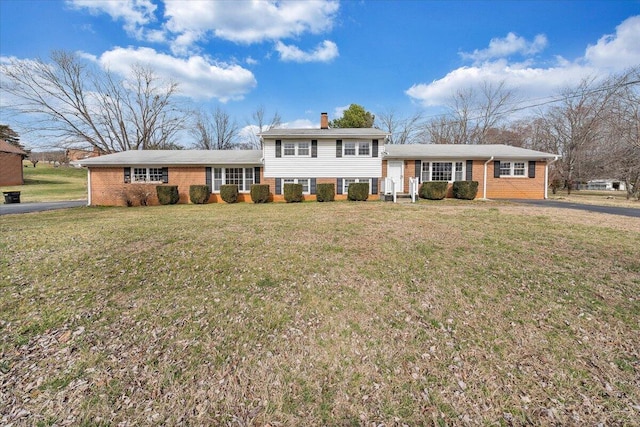 split level home with brick siding, a chimney, and a front yard