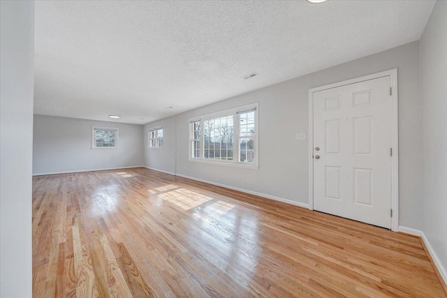 interior space with light wood-type flooring, visible vents, a textured ceiling, and baseboards