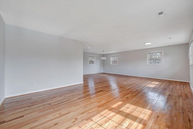 empty room with a textured ceiling, light wood finished floors, visible vents, and baseboards