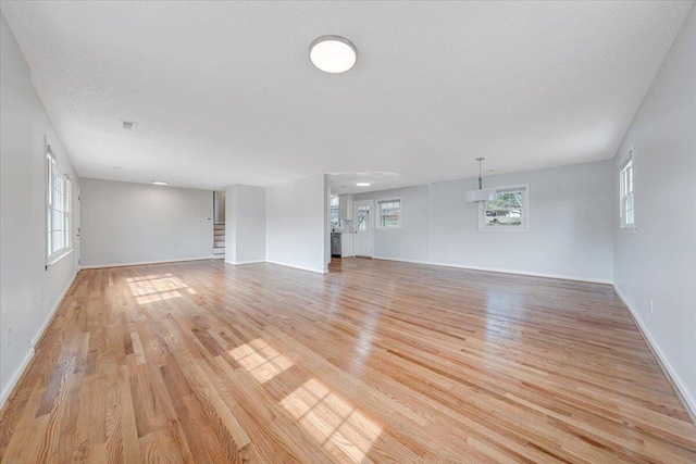 unfurnished living room with a textured ceiling, light wood finished floors, stairway, and a wealth of natural light