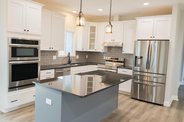 kitchen with light wood finished floors, stainless steel appliances, white cabinetry, a sink, and under cabinet range hood