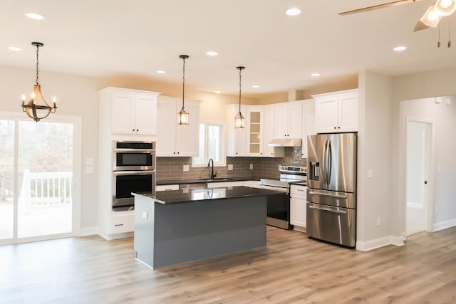 kitchen with tasteful backsplash, dark countertops, appliances with stainless steel finishes, a center island, and under cabinet range hood