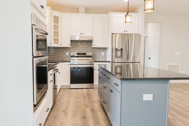 kitchen with tasteful backsplash, appliances with stainless steel finishes, a center island, light wood-type flooring, and under cabinet range hood