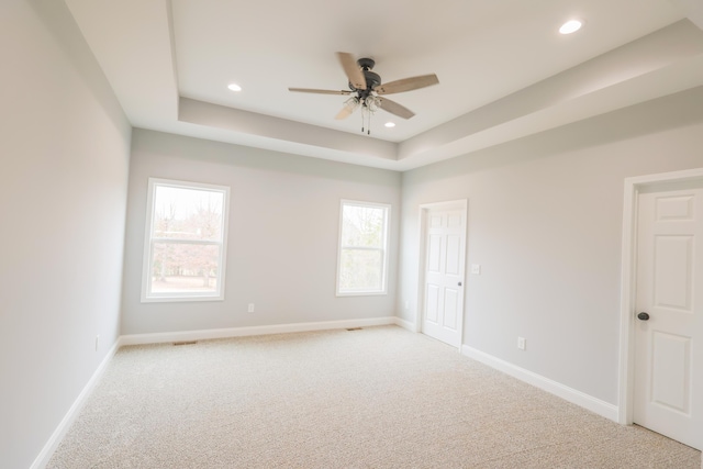 unfurnished room with a tray ceiling, recessed lighting, light carpet, ceiling fan, and baseboards