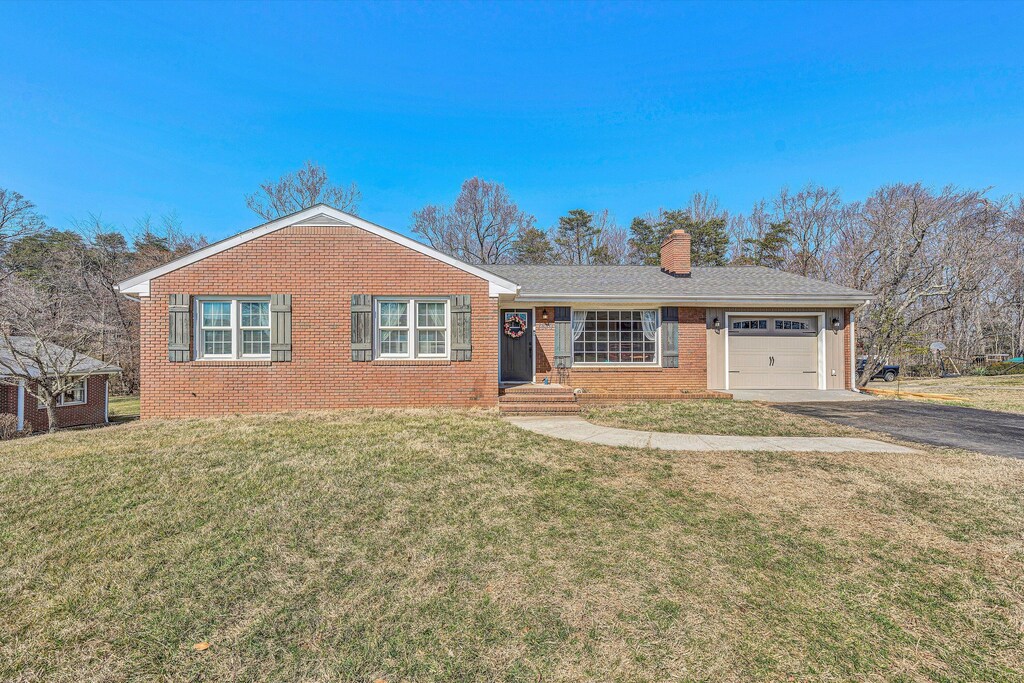 ranch-style house with an attached garage, brick siding, driveway, roof with shingles, and a chimney