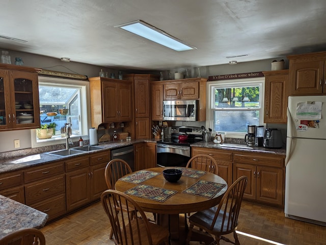 kitchen featuring brown cabinets, dark countertops, appliances with stainless steel finishes, glass insert cabinets, and a sink