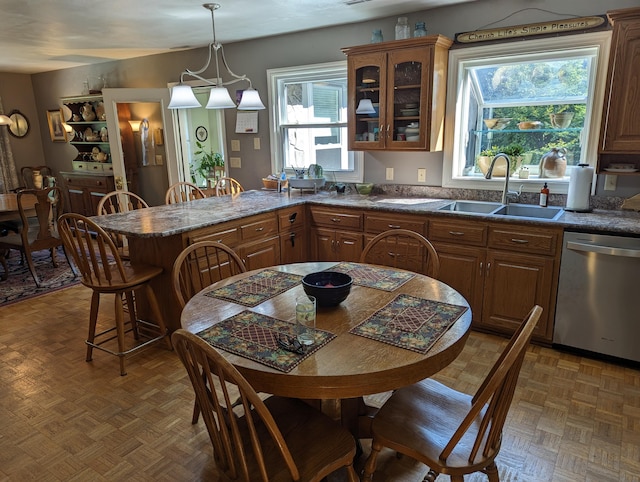 kitchen with brown cabinetry, glass insert cabinets, a peninsula, stainless steel dishwasher, and a sink