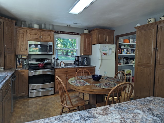 kitchen featuring appliances with stainless steel finishes, brown cabinetry, and light stone countertops