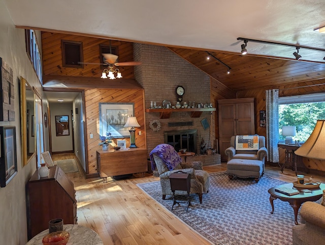 living area with ceiling fan, high vaulted ceiling, wood walls, a fireplace, and light wood finished floors