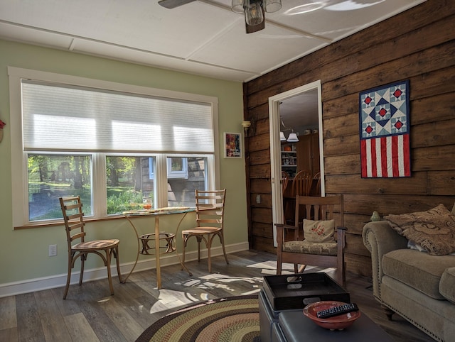 interior space with a ceiling fan, wooden walls, baseboards, and wood finished floors