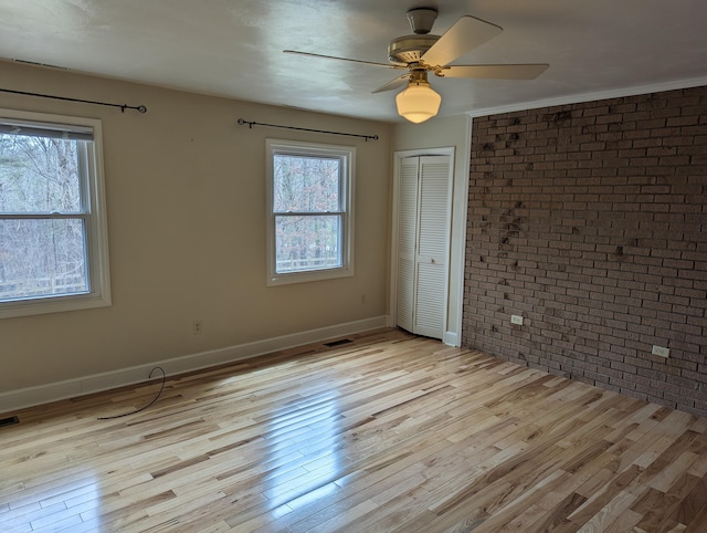 empty room featuring visible vents, ceiling fan, brick wall, wood finished floors, and baseboards