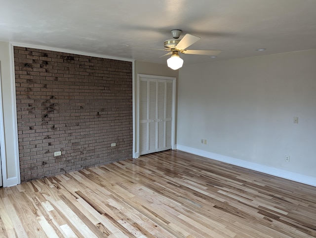 spare room with brick wall, wood finished floors, a ceiling fan, and baseboards