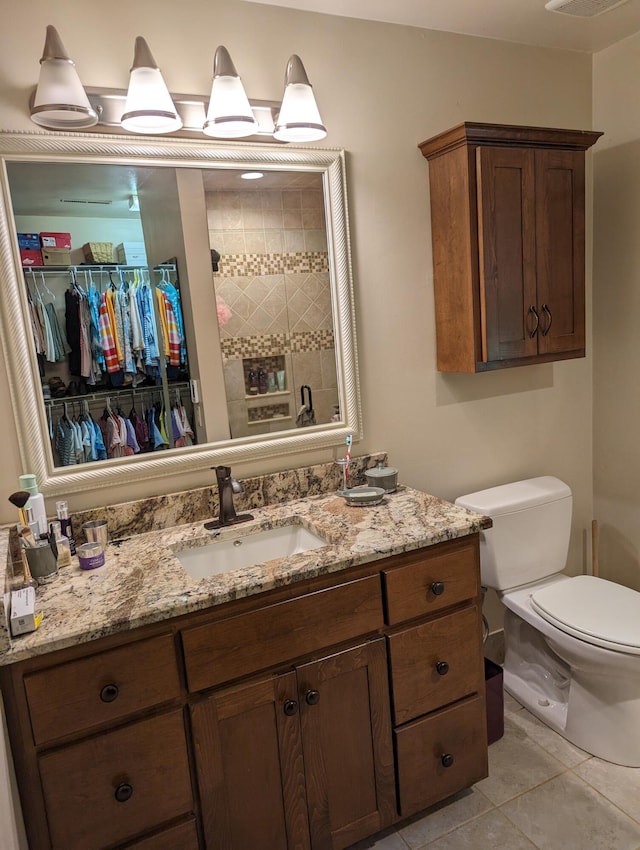 bathroom with toilet, a tile shower, vanity, and tile patterned floors