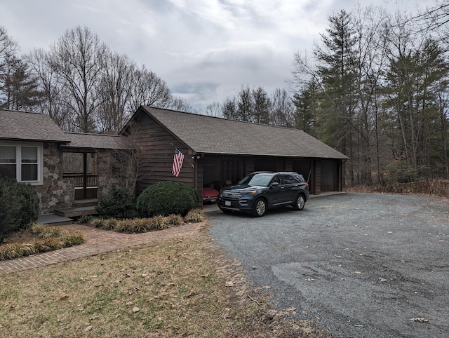 view of side of property with a garage, stone siding, and roof with shingles