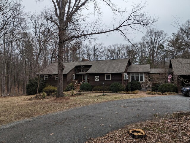 view of front of house with aphalt driveway, stone siding, a shingled roof, and a chimney