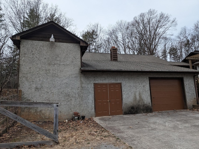 exterior space featuring a chimney, stucco siding, a shingled roof, an attached garage, and driveway