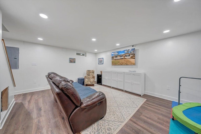 living area featuring recessed lighting, electric panel, baseboards, and wood finished floors