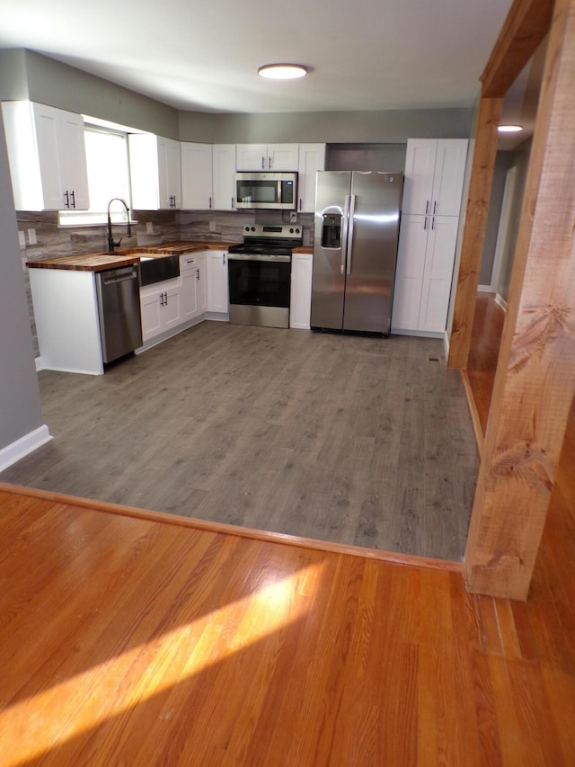 kitchen with a sink, appliances with stainless steel finishes, wood finished floors, and white cabinets