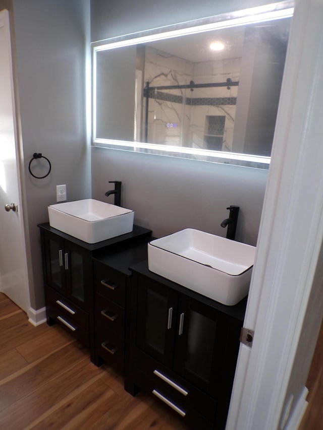 full bathroom with double vanity, wood finished floors, a stall shower, and a sink