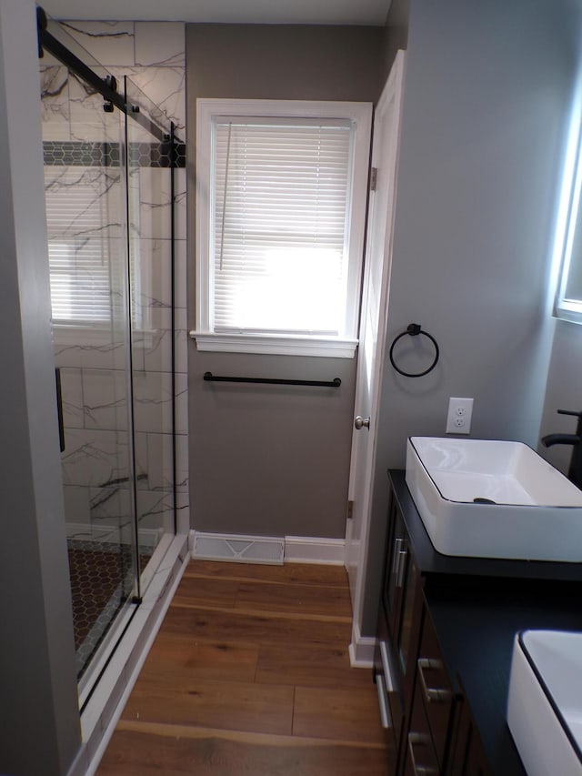 bathroom with wood finished floors, visible vents, vanity, baseboards, and a marble finish shower