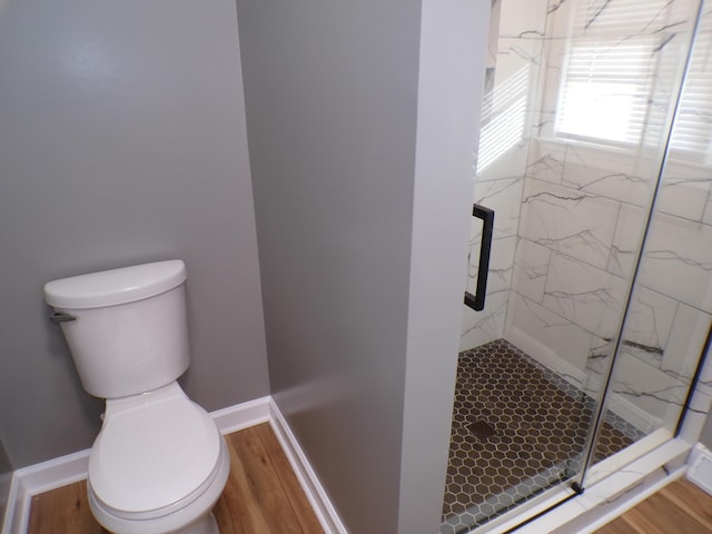 bathroom featuring baseboards, toilet, a marble finish shower, and wood finished floors