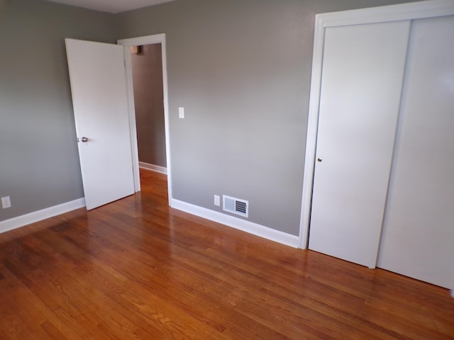 unfurnished bedroom with a closet, wood finished floors, visible vents, and baseboards