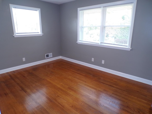 empty room with dark wood-style flooring, visible vents, and baseboards