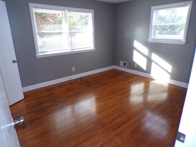 empty room featuring baseboards, wood finished floors, visible vents, and a healthy amount of sunlight