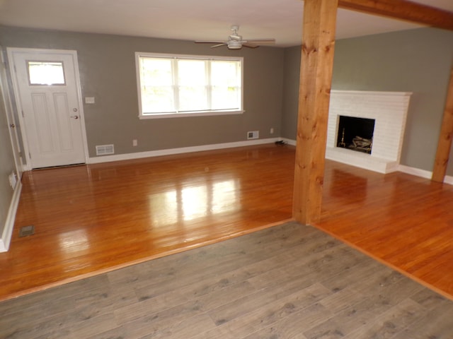 unfurnished living room featuring visible vents, a brick fireplace, ceiling fan, wood finished floors, and baseboards