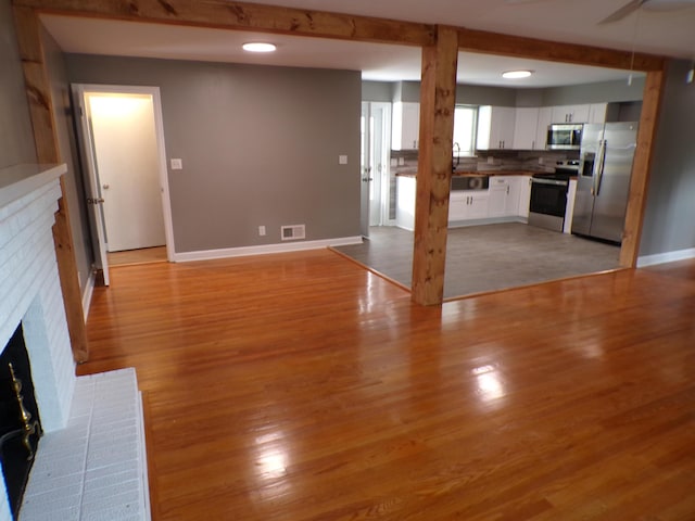 unfurnished living room with visible vents, baseboards, a brick fireplace, beam ceiling, and light wood finished floors