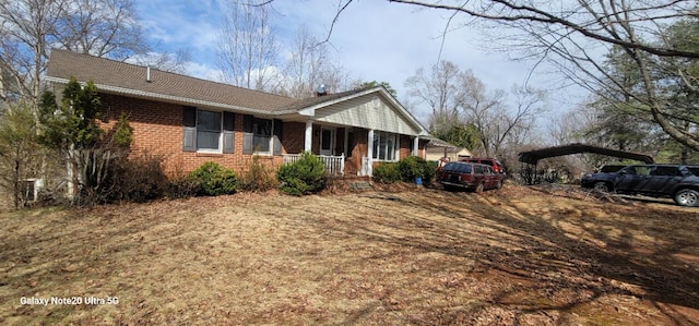 view of side of home featuring a detached carport, covered porch, and brick siding