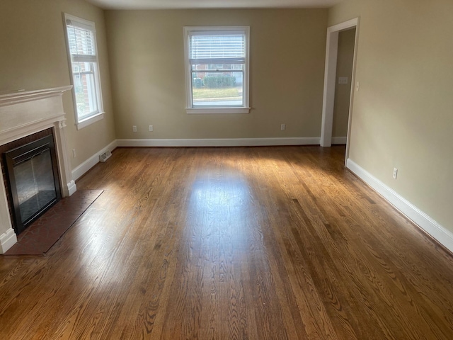 unfurnished living room featuring a wealth of natural light, a glass covered fireplace, baseboards, and wood finished floors