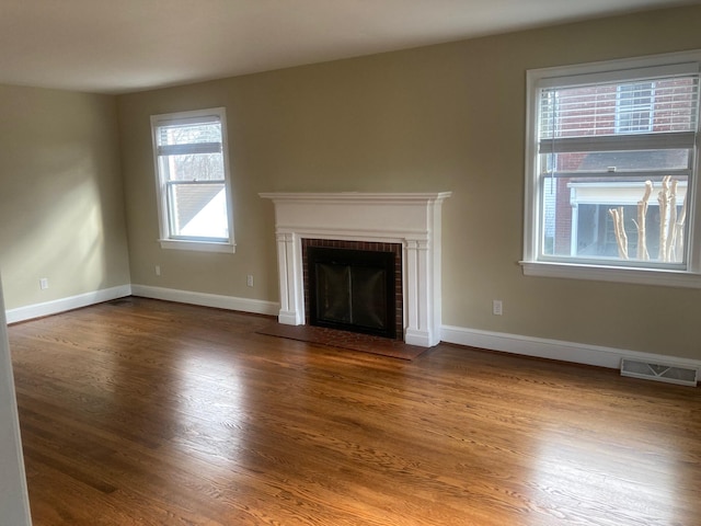 unfurnished living room with a fireplace, wood finished floors, visible vents, and baseboards