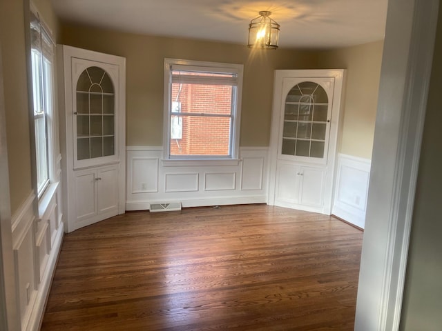 unfurnished dining area with dark wood-style floors, visible vents, and a wainscoted wall