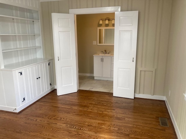 spare room with dark wood-type flooring, a sink, visible vents, baseboards, and built in features