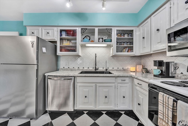 kitchen with dark floors, stainless steel appliances, a sink, white cabinetry, and glass insert cabinets