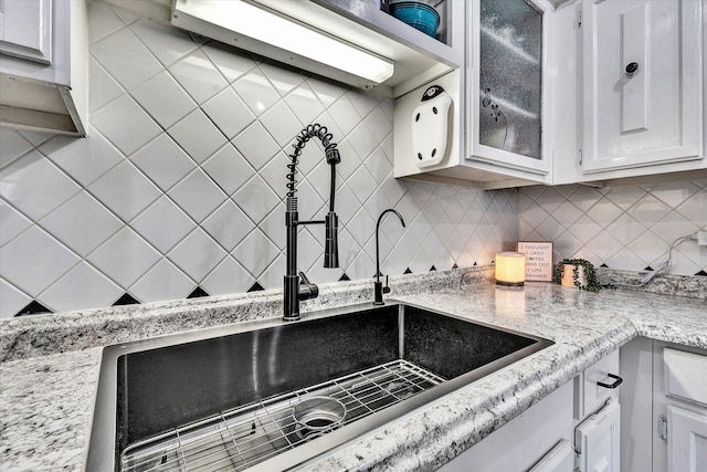 kitchen with glass insert cabinets, white cabinetry, backsplash, and a sink