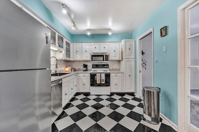 kitchen featuring dark floors, stainless steel appliances, a sink, white cabinets, and decorative backsplash