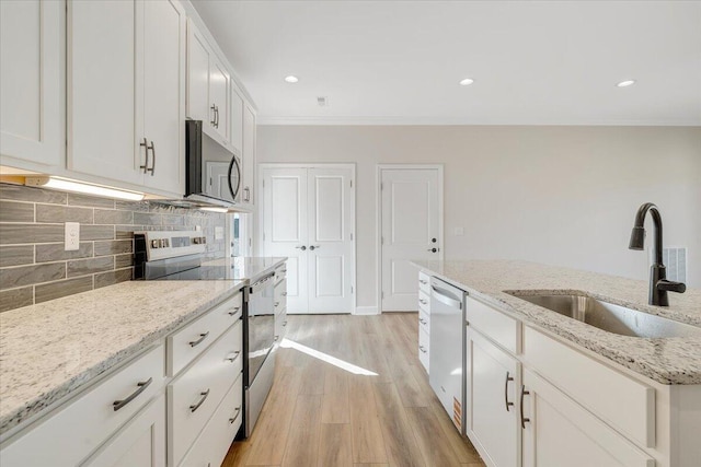kitchen with tasteful backsplash, ornamental molding, stainless steel appliances, light wood finished floors, and a sink