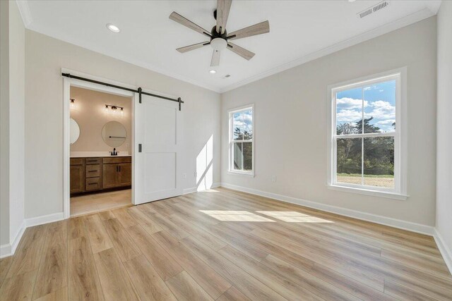 unfurnished bedroom with visible vents, light wood-type flooring, a barn door, and multiple windows