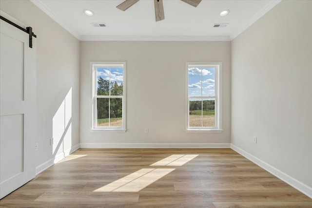 empty room with a barn door, visible vents, baseboards, and ornamental molding