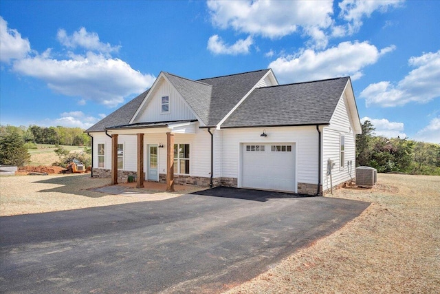modern inspired farmhouse featuring a shingled roof, stone siding, a garage, cooling unit, and driveway